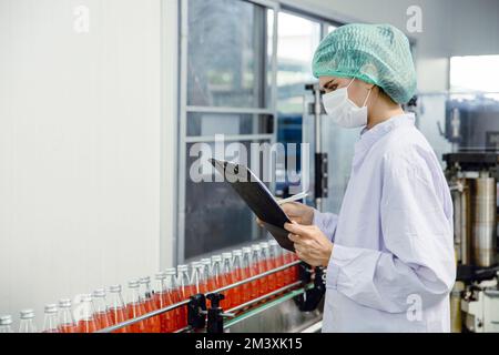 food and drink industry staff worker working at conveyor belt production line machine in beverage factory with clean and hygiene area. Stock Photo