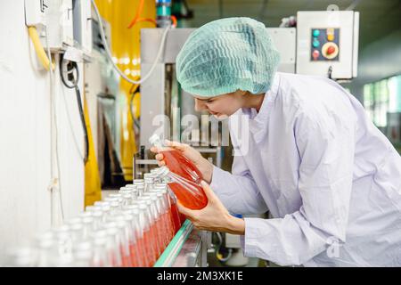 food and drink industry staff worker working at conveyor belt production line machine in beverage factory with clean and hygiene area. Stock Photo