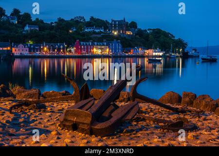 Anchors on the quayside with the colourful lights of the waterfront reflected in the still water of Tobermory harbour, Isle of Mull, Scotland, UK Stock Photo