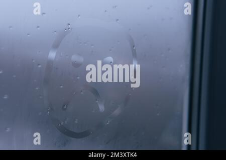 Unhappy, sad emoji on foggy glass window. Face sign close-up. Selective focus on photo. Depression and sadness concept. Stock Photo