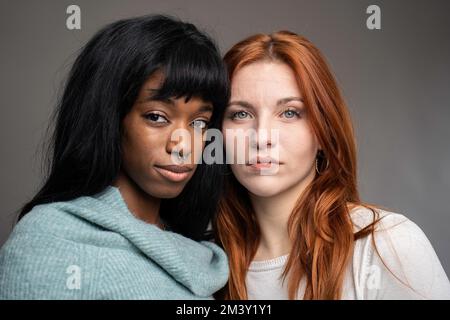 Couple of young women of different ethnicities - Red headed Caucasian woman with African female partner pose looking at camera - Multiculturalism and Stock Photo