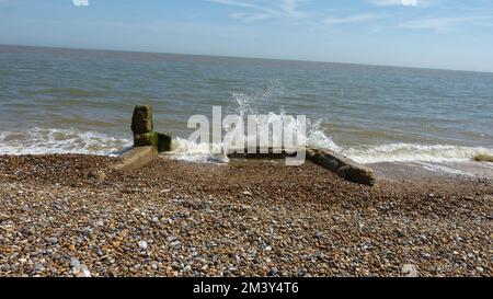 White spray from wave breaking over remains of World War II Pillbox Defence, that has fallen from the top of the cliff at Thorpeness, 15th June 2022 Stock Photo