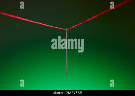 Steel needle hangs on a red thread against graduated green background. Stock Photo