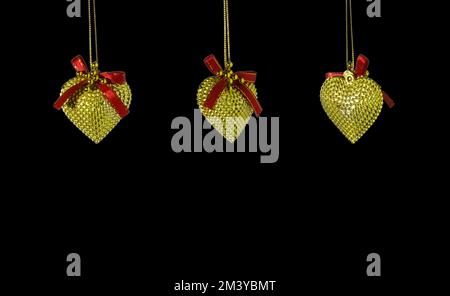 three golden heart ornaments hanging from the top of a black background, a creative holiday concept Stock Photo