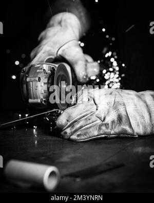 A grayscale shot of a person using a sander tool on a metal Stock Photo
