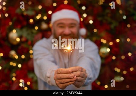 focus on hands with bengal fire and beard man in santa hat Christmas tree background. Merry Christmas and Happy New Year celebration Stock Photo