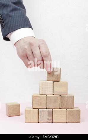 Hand creating pyramid from wooden cubes Stock Photo