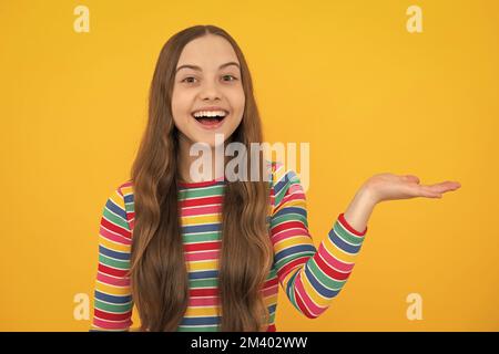 Look at advert. Teenager child points aside shows blank copy space for text promo idea presentation, poses against yellow background. Stock Photo