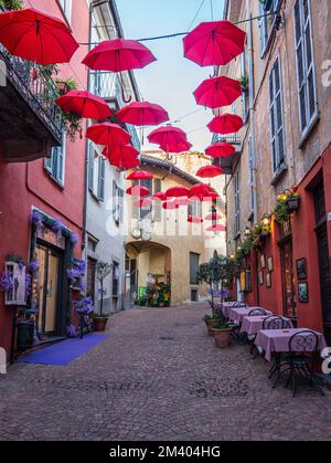 luino, Italy - 12-06-2022: Beautiful street in the historic center with colorful shops and hanging red umbrellas in Luino Stock Photo