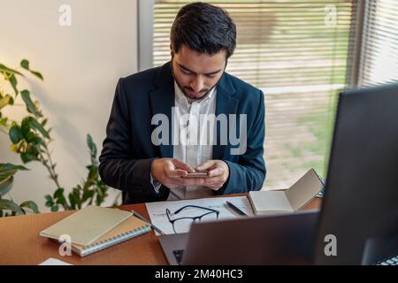Focused indian businessman in suit use phone while working from home office  Stock Photo