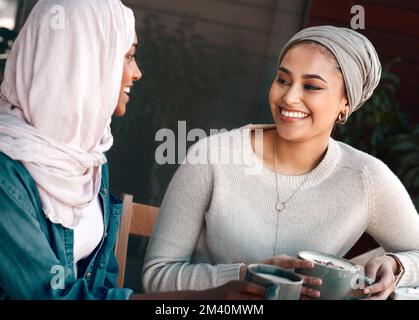 You always have the juiciest stories. two affectionate young girlfriends having a chat at a coffee shop while dressed in hijab. Stock Photo