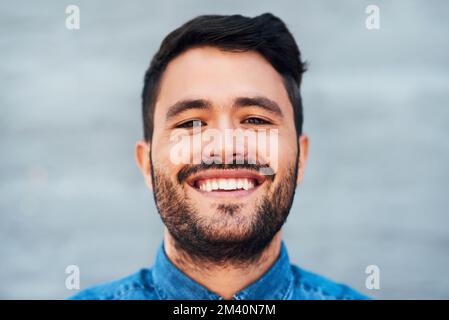 Just a carefree bearded man. Closeup portrait of a handsome young man smiling while standing against a brick wall. Stock Photo