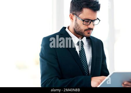 Businessmen do things using apps nowadays. a handsome young businessman using a digital tablet while standing in a modern office. Stock Photo