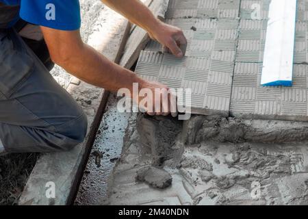 Bricklayer lays tiles on cement. Photo of hand with tile close-up. Authentic workflow. Construction background.. Stock Photo