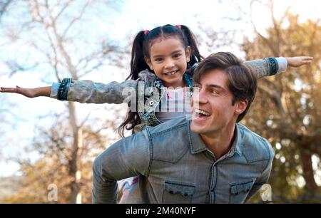Lets fly to the moon and back. an adorable little girl enjoying a piggyback ride with her father at the park. Stock Photo