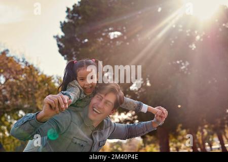Catching a flight on Daddy Airlines. an adorable little girl enjoying a piggyback ride with her father at the park. Stock Photo