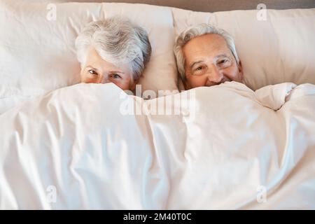 Staying young at heart with a little hide and seek. a playful senior couple hiding under the covers while in bed together in a nursing home. Stock Photo