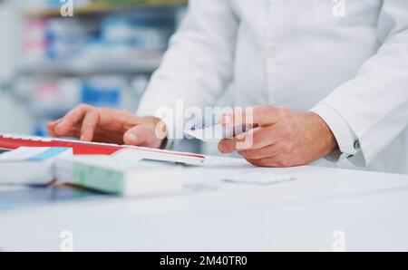 Im extra careful when distributing dosages. a pharmacist holding medication while typing on a computer. Stock Photo