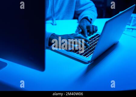 Hes letting his fingers do all the talking. an unrecognizable hacker using a laptop in the dark. Stock Photo