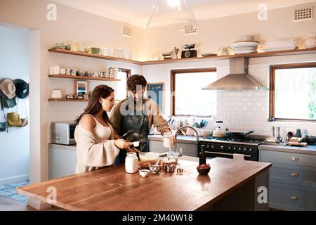 Bake your home a happy place. a young couple using a digital tablet while preparing breakfast at home. Stock Photo