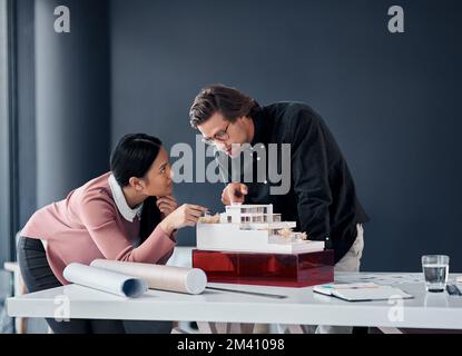 Things are coming together perfectly. two young architects working together on a scale model of a modern house in their office. Stock Photo