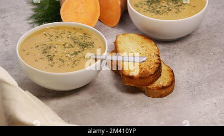 sweet potato puree soup in white bowl with garlic bread on grey marble table Stock Photo