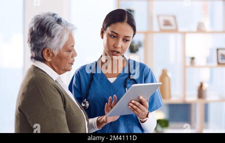 Taking her through her diagnosis. a young doctor using a digital tablet during a consultation with a senior woman. Stock Photo