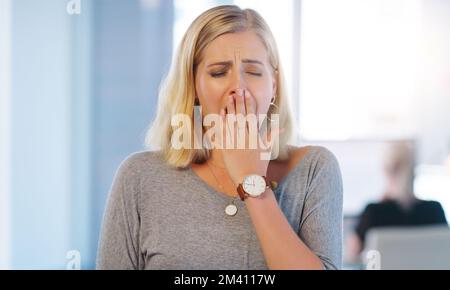 Its been a long day. a tired looking young businesswoman holding her hand in front of her mouth after yawning inside of the office. Stock Photo