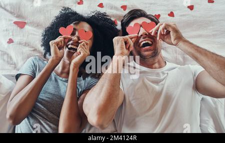 Weve got love in sight. High angle shot of a young couple covering their faces with heart shaped decorations in their bedroom at home. Stock Photo