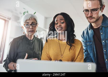 Getting their opinion. three creative businesspeople working together on a laptop in their office. Stock Photo