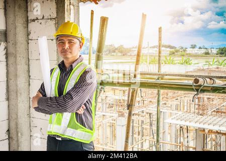 Asian business man construction engineer worker in protective helmet and blueprints paper on hand at building site Stock Photo