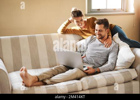 Were relaxed and entertained. a young couple using a laptop while relaxing at home. Stock Photo