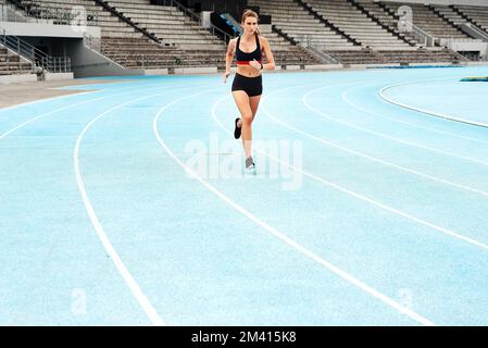 Sometimes all you need is a good, long run. Full length shot of an attractive young athlete running a track field alone during a workout session Stock Photo
