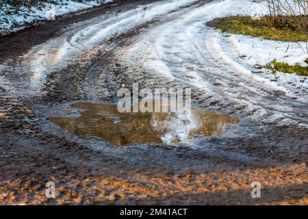 Small puddle on the road, reflection in water near the meadow. Snow and winter Stock Photo