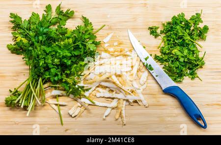 Parsley placed on the wooden desk with the knife near. Sharpened parsley prepared for cooking. Fresh and healthy plant. Stock Photo