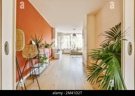 a living room with an orange accent wall and wooden flooring in the center of the room, there is a large plant on Stock Photo