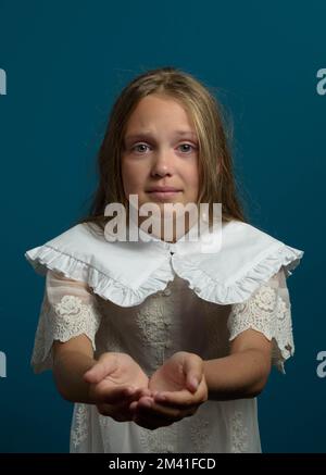 Unhappy child. Need help emotion. Long hair well dressed young girl with pitiful look and hands begging for aid. Dark blue background Stock Photo