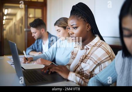 University, education and group of students at desk doing project, studying and learning with laptop and notebook. Academy, college and young people Stock Photo
