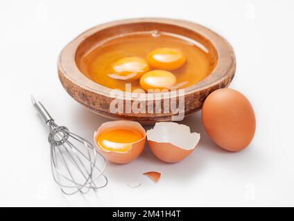 Three egg yolks in wooden plate on white with shell and whisk Stock Photo