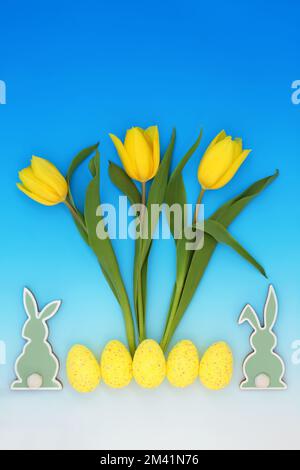 Happy Easter celebration abstract concept with yellow  Easter eggs, tulip flowers, bunnies. Holiday symbols on gradient blue white background. Stock Photo