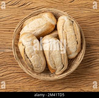 Whole grain french bread, salt bread or pistolet in a basket over wooden table. Stock Photo