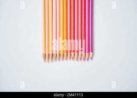 Raw of warm colored pencils paced in gradient from beige to violet over white background. Close up. Stock Photo