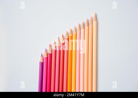 Diagonal raw of warm colored pencils paced in gradient from beige to violet over white background. Close up. Stock Photo