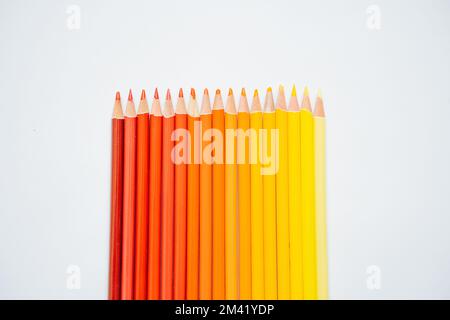 Gradient raw of warm colored pencils paced from yellow to red over white background. Close up. Stock Photo