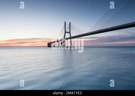 Background with colourful sunrise on the Lisbon bridge. The Vasco da Gama Bridge is a landmark, and one of the longest bridges in the world. Urban lan Stock Photo