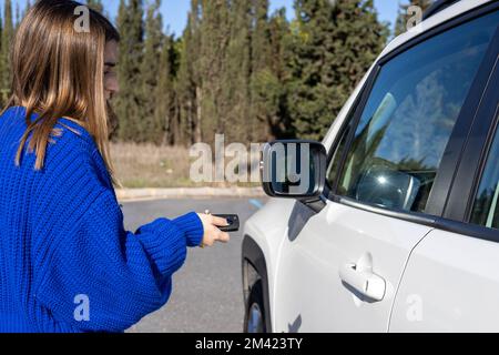 women hand presses on the remote control car alarm systems.Women hand pressing the button on the remote to lock or unlock the red car, travel concept Stock Photo