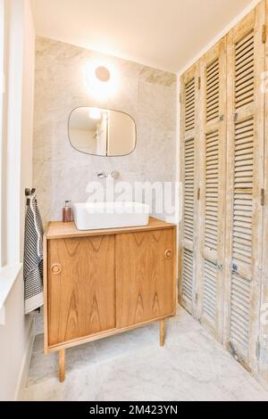 a bathroom with wooden shutters on the wall and white marble flooring in the shower stall is next to the sink Stock Photo