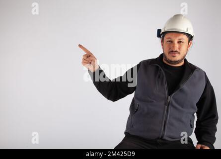 Man with white safety helmet pointing empty text area on isolated white background. Stock Photo