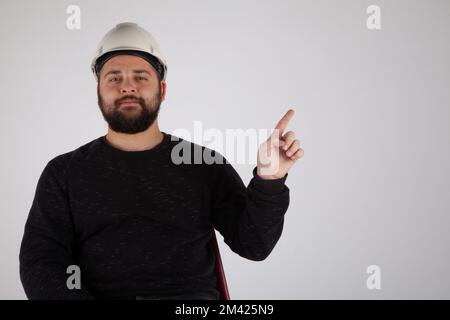 Man with white safety helmet pointing empty text area on isolated white background. Stock Photo
