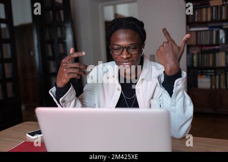 Smiling young African man tutor wearing wireless earbuds talking by webcam teaching online from home Stock Photo